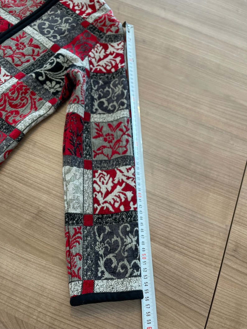 May include: A red, black, and white patterned jacket with a zipper closure. The sleeve is measured with a tape measure, showing a length of 58 cm.
