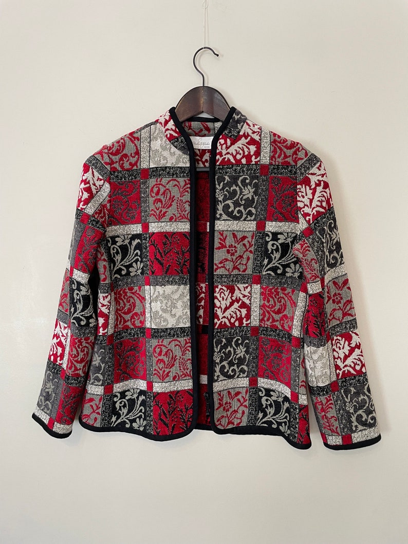 May include: A red, black, and white patterned jacket with a mandarin collar and a black trim. The jacket is made of a woven fabric and has a front closure.