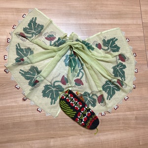 Könnte beinhalten: Ein hellgrüner Schal mit einem floralen Muster aus grünen Blättern und roten Blüten und einem gehäkelten Rand. Eine schwarz, rot und grün gemusterte Socke ist ebenfalls im Bild. Der Schal ist gefaltet und gebunden.