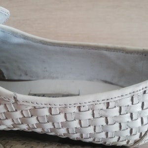 May include: Close-up of a white woven leather shoe. The shoe's interior is visible, showing the insole and the inside of the upper. The woven pattern is detailed and covers the front and side of the shoe.