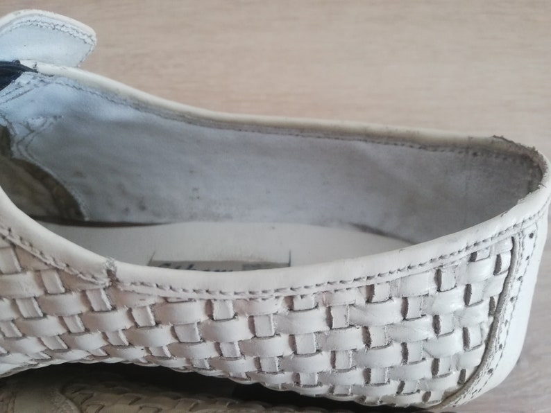 May include: Close-up of a white woven leather shoe. The shoe's interior is visible, showing the insole and the inside of the upper. The woven pattern is detailed and covers the front and side of the shoe.