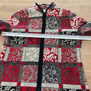 May include: A red, black, and white patterned jacket with a zipper closure. The jacket has a mandarin collar and a black trim around the collar and zipper.
