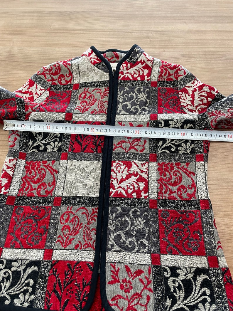 May include: A red, black, and white patterned jacket with a zipper closure. The jacket has a mandarin collar and a black trim around the collar and zipper.