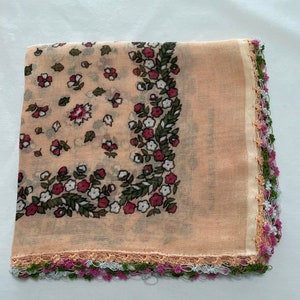 May include: A peach-colored square scarf with a floral print and a crocheted border in shades of green, pink, and white.