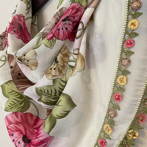 May include: White floral scarf with a green and yellow crocheted border. The scarf has a label that says "Emba Ipek".