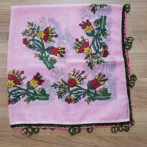 May include: A pink square scarf with a green crocheted border. The scarf has a floral pattern with yellow, red, and green flowers.