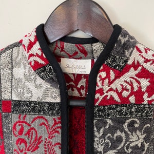 May include: A black zippered jacket with a patchwork design featuring red, gray, and white floral patterns. The label reads "Studio Works Petite."