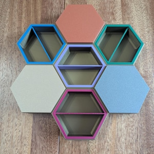 May include: A set of seven hexagonal shelves in various colors, including blue, coral, green, lavender, beige, and light blue. Each shelf has a dark interior and a colored border, arranged in a honeycomb pattern on a wooden surface.