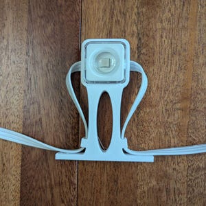 Könnte beinhalten: Eine weiße LED-Leuchte mit quadratischem Leuchtengehäuse und Halterung. Die Leuchte hat eine klare Linse und ist mit weißen Drähten verbunden. Die Leuchte ist auf einer Holzoberfläche montiert.