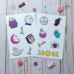 May include: Two sheets of clear stickers with a variety of witchy and magical designs. The stickers include a cauldron, a crystal ball, a skull, a crystal, a potion bottle, a hand with a crescent moon, an eye, a crescent moon, a book with a star, a witch's hat, and a crescent moon with three stars.