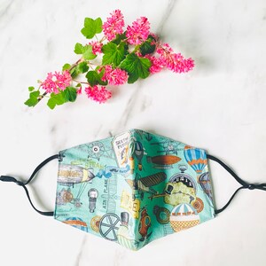 May include: A turquoise blue face mask with a white and black print of a vintage airship, airplane, and other steampunk-inspired designs. The text "See the Future" is printed on the mask.