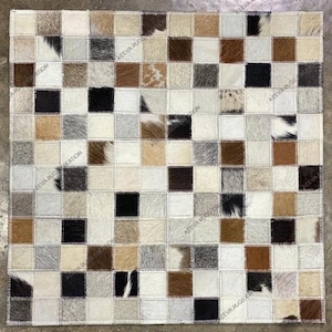 May include: Square patchwork rug featuring a checkerboard pattern of various natural hide squares. The squares are in shades of white, black, brown, and tan, creating a textured and visually interesting design. The rug is a decorative floor covering.