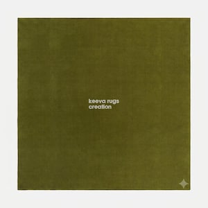 May include: A square olive green rug with a smooth, uniform texture. The text "keeva rugs creation" is printed in white in the center. A small, white, four-pointed star icon is located in the bottom right corner of the rug surface.