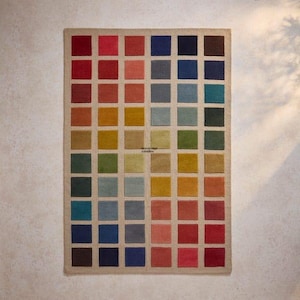 May include: A rectangular rug featuring a grid design of coloured squares. The squares are in shades of red, orange, yellow, green, blue, and brown. The rug has a neutral border.
