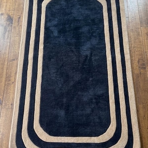 May include: A rectangular area rug with rounded corners featuring a solid dark navy blue center surrounded by alternating concentric bands of beige and dark navy blue. The rug has a plush, textured pile surface and a clean, geometric border design.