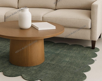 May include: A round wooden coffee table with a white vase and a stack of books sits in front of a beige sofa. A green, scalloped-edge rug is on the floor, adding a touch of color and texture to the living room setting.