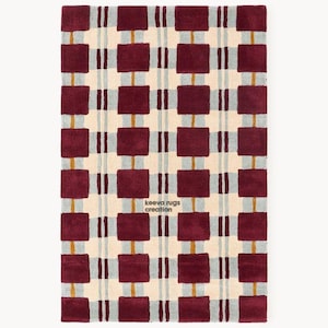 Op de afbeelding: Een rechthoekig vloerkleed met een herhalend patroon van bordeauxrode vierkanten en verticale lijnen tegen een crèmekleurige achtergrond. Het ontwerp bevat lichtgrijze en gouden accenten. De tekst "keeva rugs creation" is zichtbaar.