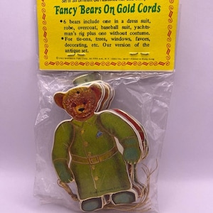 May include: A package of six vintage paper bear ornaments with gold cords. The bears are dressed in different outfits, including a suit, robe, and baseball uniform. The package says "Fancy Bears On Gold Cords".