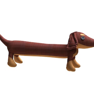 Puede incluir: Un animal de peluche con forma de dachshund marrón y beige con un botón para el ojo.