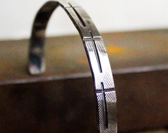 May include: A silver bracelet with a geometric design. The bracelet is made of a thin metal band with a series of parallel lines etched into the surface.