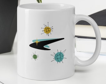 May include: White ceramic mug with a mid-century modern design featuring a black and blue abstract shape with yellow, green, and blue starbursts.