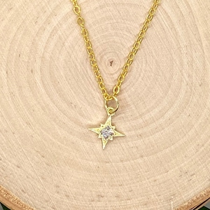 Può includere: Una collana con catena dorata e un piccolo ciondolo a forma di stella scintillante.