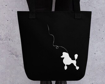 May include: A black tote bag with a white silhouette of a poodle on a leash. The bag has long handles and is being held by a person.