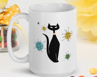 May include: White ceramic mug with a black cat illustration and colorful mid-century modern style starbursts. The cat is wearing a yellow collar.