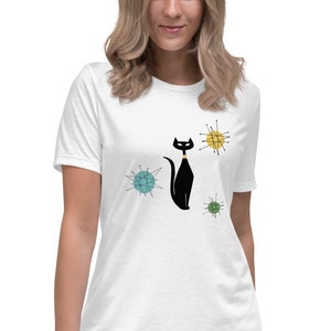 May include: A white t-shirt featuring a black cat with a gold collar, surrounded by colourful mid-century modern atomic starburst designs.