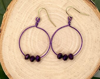 May include: A pair of purple hoop earrings with three dark purple beads on each hoop.