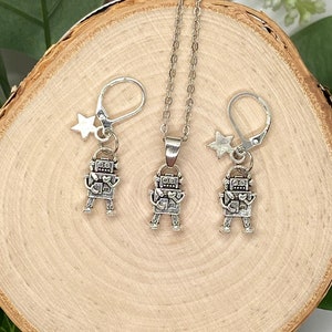 May include: A silver robot charm necklace and earrings set. The necklace and earrings feature a small robot charm with a heart on its chest and a star charm.