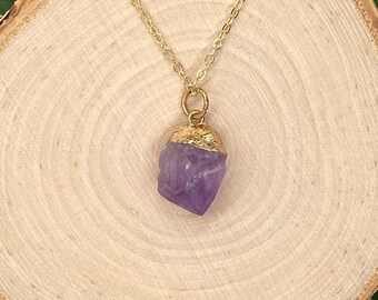 May include: A gold chain necklace with a purple amethyst crystal pendant. The crystal is raw and has a natural, irregular shape.