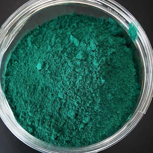 Può includere: Una vista ravvicinata di un barattolo di vetro pieno di una polvere verde brillante. La polvere è finemente macinata e ha una consistenza uniforme.