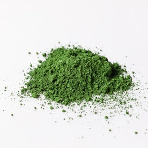 Può includere: Un mucchio di polvere verde su uno sfondo bianco. La polvere è finemente macinata e ha una consistenza liscia.