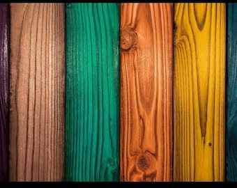 May include: Six vertical wooden planks arranged side by side, each featuring a distinct stained finish in purple, natural light brown, green, orange, yellow, and blue, showcasing visible wood grain patterns and natural knots.