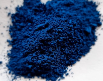 May include: A close-up of a pile of bright blue pigment powder. The powder is finely ground and has a smooth, velvety texture.