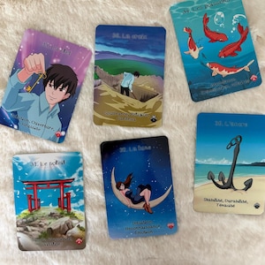 May include: Six tarot cards with vibrant illustrations. The cards depict a key, a cross, koi carp, a sun, a woman on a crescent moon, and an anchor. Each card has a title and keywords in French, with a soft, fluffy background.