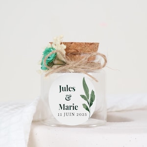 Peut inclure: Un petit bocal en verre avec un couvercle en liège et une étiquette blanche. L'étiquette a des feuilles vertes et le texte "Jules & Marie 11 JUIN 2025".