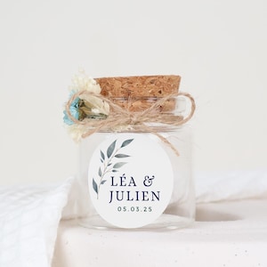 Könnte beinhalten: Ein kleines Glasgefäß mit einem Korkverschluss und einem weißen Etikett. Das Etikett zeigt ein blaues und grünes Blumenmuster und den Text "LÉA & JULIEN 05.03.25".