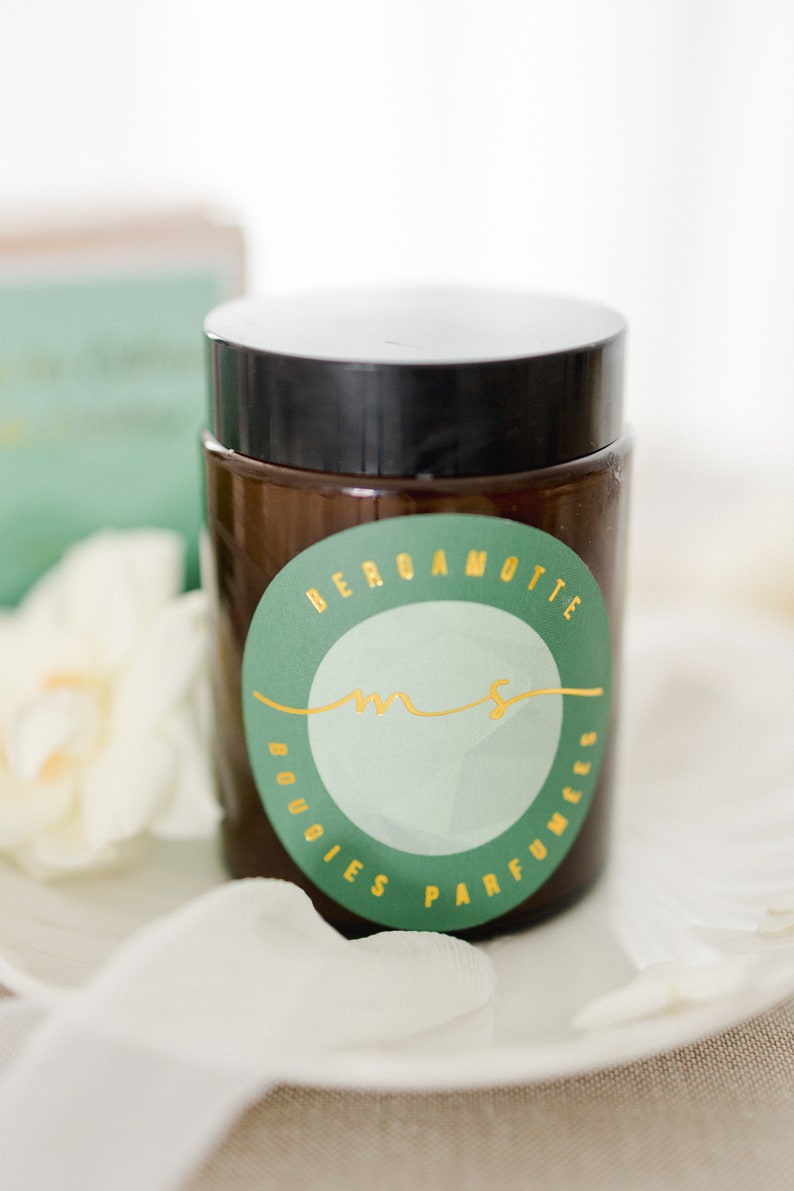 May include: A brown glass jar with a black lid and a green and gold label that says "Bergamotte Bougies Parfumees".