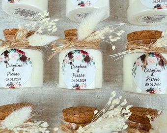 Könnte beinhalten: Ein Set kleiner Glasgefäße mit Korkdeckeln, gefüllt mit weißen Kerzen. Jedes Gefäß ist mit einem Blumendesign und einem personalisierten Etikett verziert, auf dem "Caroline & Pierre 09.04.2024" steht.