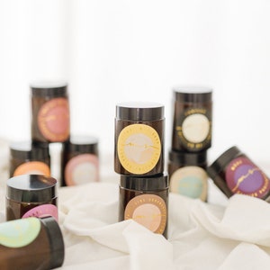 May include: A collection of brown glass candle jars with gold labels. The labels feature a circular design with a handwritten logo and the words "Citrus & Mint" and "Pumpkin Spice" are visible.