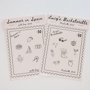 May include: Two beige paper cards with black line drawings and text. One says "Summer in Spain girls trip 2025" and the other says "Lucy's Bachelorette Nashville 2025". Each card has a stamp-like border and illustrations.