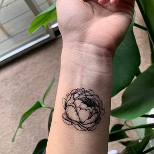 May include: A black and white temporary tattoo of a peony flower on a person's wrist.