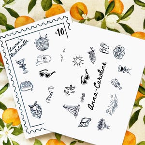 Puede incluir: Dos tarjetas blancas con ilustraciones de línea negra de objetos con temática de vacaciones, que incluyen una bola de discoteca, gafas de sol y un velero. Una tarjeta dice "Lauren's Bachelorette" y la otra "Anna-Caroline". El fondo es una tela floral.