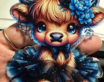 May include: A cute cartoon highland cow wearing a blue tutu with a blue flower crown. The cow has big blue eyes and a pink nose.