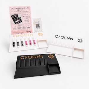 May include: Display stands in white and black, with the word "CHOGAN" in gold. The stands are designed to hold lipsticks and have a small tray. A sign reads "LIEBLINGSPARFUM LEER?" with additional text.