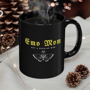 Op de afbeelding: Zwarte koffiemok met een gele afbeelding waarop staat "Emo Mom Not a Regular Mom" en een zwart-witte vlinder met een halve maan ontwerp.