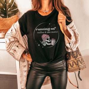 May include: Black t-shirt featuring a graphic of a skull wearing a pink beanie and holding a coffee cup. The graphic is enclosed in a circle with the text "running on coffee & emo music".