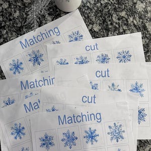 May include: A set of printable snowflake matching and cutting activity sheets. The sheets have the words "Matching" and "Cut" printed on them. The snowflakes are blue and white.